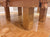 Close-up of a rustic wooden table with thick block legs and carved decorative ends, shown in a real room with a polished wood parquet floor.