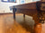 A close-up view of a wooden billiards pool table in a home interior with tiled floors and framed wall art.