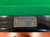 Close-up of a billiards table featuring a green felt playing surface, a glossy black wooden rail, and a rectangular bronze-colored metal plaque with the text 'Fiegence' and 'Canada Billiards & Bowling'.
