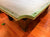 A close-up view of a green-felted billiards table corner with dark wooden legs, set on a polished reddish-brown wooden floor.