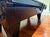 A close-up view of a dark brown wooden pool table corner with decorative carved panels and a polished hardwood floor in the background.