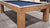 Wooden pool table with a blue felt surface on a concrete floor.