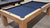 Pool table with blue felt surface and wooden frame on a tiled floor.