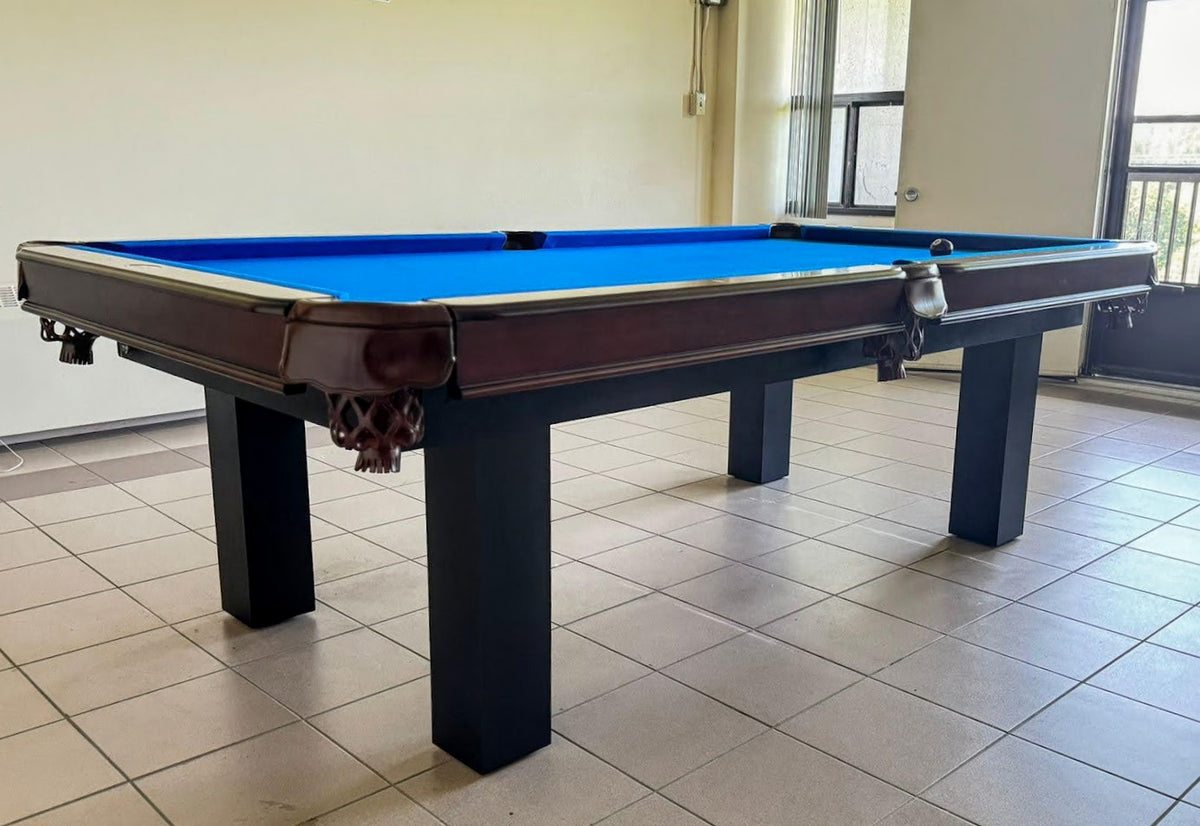 The corner view of Majestic Orleans 7-foot walnut frame and black legs pool table with leather drop pockets , blue felt in the game room
