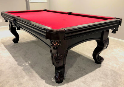 A black mahogany wood pool table with red cloth top, featuring carved leg designs and leather-fringed pockets.