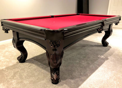 A  mahogany wood pool table with red cloth top, featuring carved leg designs and leather-fringed pockets.