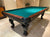 An 8' Majestic Pinnacle Two Tone Walnut Pool Table with green cloth, showing the table from the long end with the Majestic brand logo on the corner pocket.