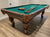 Billiard table in brown walnut finishing with green felt and balls and cues on the top.